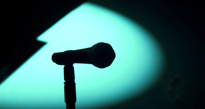 Mikrofon i strålkastarens sken på tom scen. Foto: JF Sebastian/Flickr (CC)